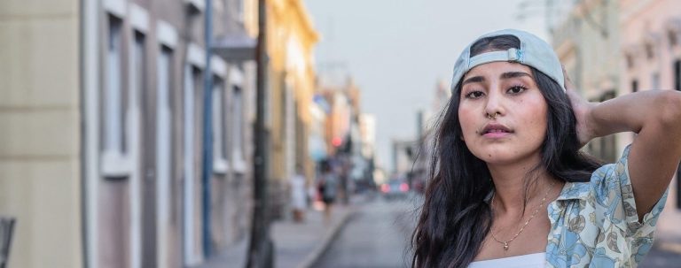 young hispanic woman wearing a backward ball cap and a floral shirt standing in the street